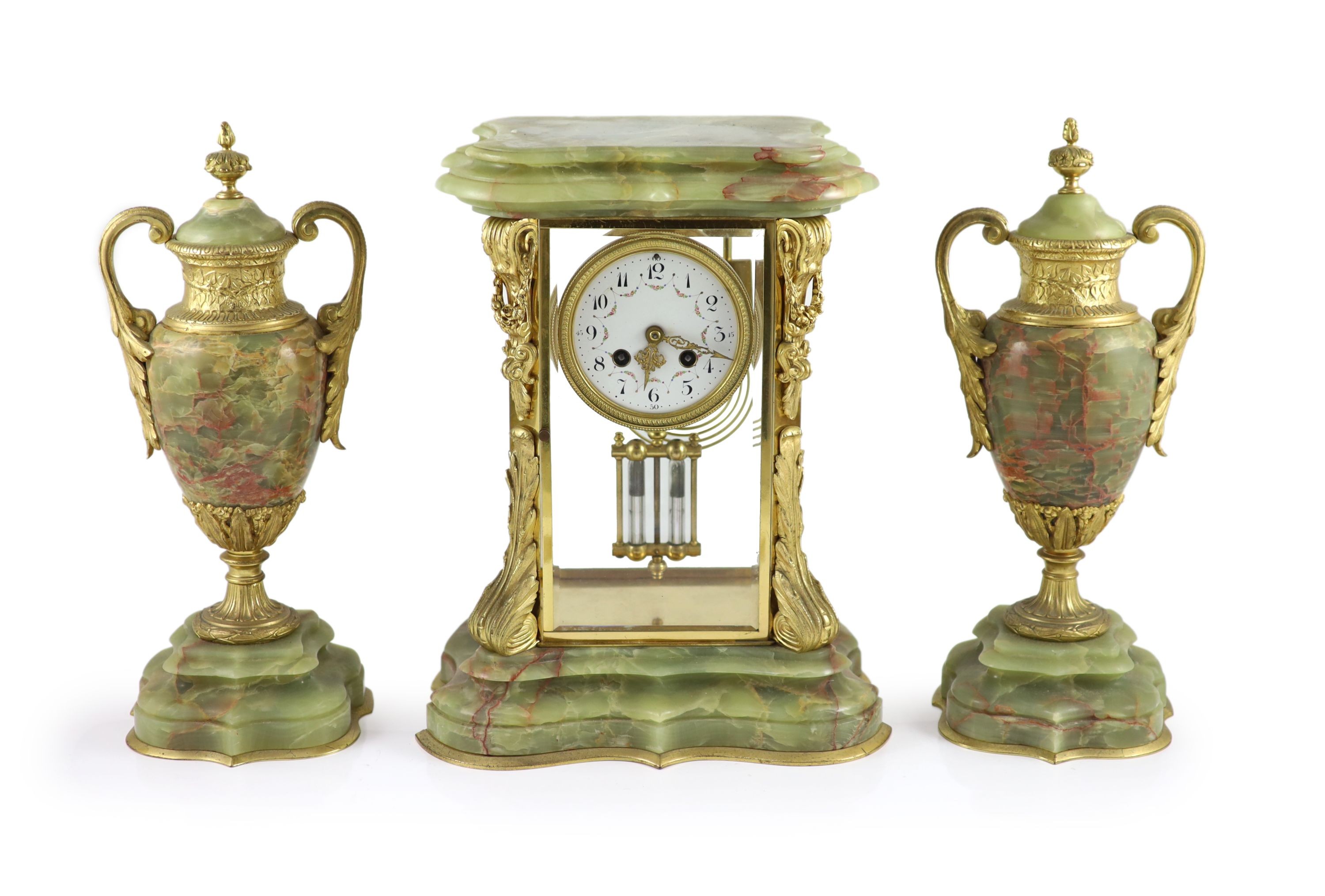 A green onyx and gilt metal clock garniture, comprising a four-glass regulator with enamelled dial in serpentine case and a pair of pedestal urns and covers Clock H 35cm. W 27cm. Urns H 36cm.